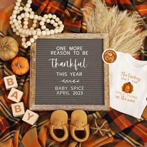 K&ouml;nnte beinhalten: Eine Baby-Ank&uuml;ndigung zum Thema Thanksgiving mit einem Buchstabenbrett, auf dem "One more reason to be thankful this year Baby Spice April 2023" steht. Au&szlig;erdem sind Holzbl&ouml;cke zu sehen, die "BABY" buchstabieren, ein Strampler mit einem Truthahn-Motiv und dem Text "The Turkey isn't the only thing in the oven" sowie kleine dekorative K&uuml;rbisse.