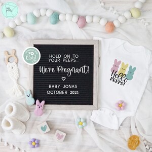 May include: A pregnancy announcement with a black letter board that reads "Hold on to your peeps... We're Pregnant! Baby Jonas October 2021". A white onesie with three pastel-colored Peeps and the text "Hello Peeps!" is next to the letter board. The onesie is surrounded by pastel-colored felt balls and flowers.