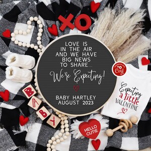 Pu&ograve; includere: Una coperta a quadri bianchi e neri con cuori rossi, un body bianco con il testo "Expecting a little Valentine" e un cartello rotondo in ardesia con il testo "Love is in the air and we have big news to share... We're Expecting! Baby Hartley August 2023".
