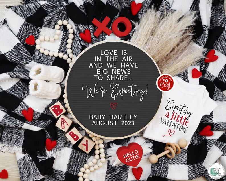 Pu&ograve; includere: Una coperta a quadri bianchi e neri con cuori rossi, un body bianco con il testo "Expecting a little Valentine" e un cartello rotondo in ardesia con il testo "Love is in the air and we have big news to share... We're Expecting! Baby Hartley August 2023".