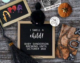May include: A black letter board with the text "I smell a child! Baby Sanderson brewing until October 2021". There is a black cat plush toy, a pumpkin, a black broom, and a framed ultrasound image with the text "Boo Sanderson".