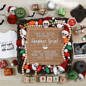 Op de afbeelding: Een baby-aankondiging met Halloween-thema met een houten bord waarop staat "We've been keeping a fangtastic secret. Baby Addams due to unwrap July 20XX". Het bord is omringd door verschillende Halloween-decoraties, waaronder pompoenen, vleermuizen en schedels.
