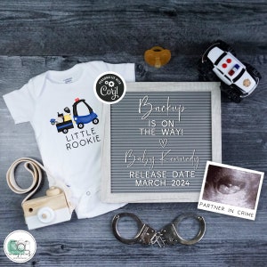 May include: A white onesie with a blue and yellow police car graphic and the text "Little Rookie". A letter board with the text "Backup is on the way!" and "Baby Kennedy Release Date March 2024". A toy police car, a pacifier, and handcuffs are also included in the image.