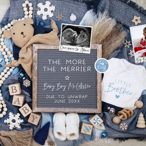 May include: A baby announcement with a letter board that reads "One more to More THE MORE THE MERRIER Baby Boy McCallster DUE TO UNWRAP JUNE 20XX". The board is surrounded by a blue blanket, a white onesie with the text "LITTLE BROTHER", a wooden toy, a wooden bead garland, a wooden block spelling "BABY", a small white ornament, a snowflake, and a framed ultrasound image.