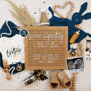 May include: A wooden sign with the text "We're Expecting 2023 to be a Great Year!" with a heart symbol, "Baby Clark #2 Due to Arrive July 202X".  The sign is surrounded by baby items including a blue and white onesie with the text "Little Brother", a wooden rattle, a blue baby blanket, a pair of brown baby booties, a wooden bunny, a wooden bottle, a wooden bead garland, and a black and white ultrasound image.