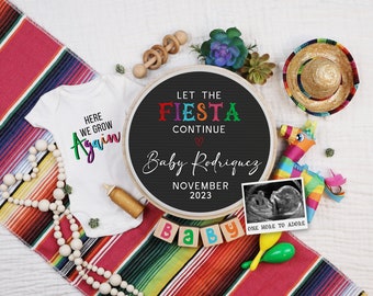 Può includere: Un cartello in ardesia nera con il testo "Let the Fiesta Continue" in lettere colorate, un cuore e le parole "Baby Rodriguez, novembre 2023". Il cartello è circondato da una varietà di decorazioni a tema messicano, tra cui un body per neonato, un sombrero, una maracas e una piñata.