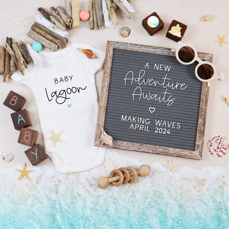 Op de afbeelding: Een witte romper met de tekst "Baby Lagoon" en een klein blauw hartje. Een letterbord met de tekst "A New Adventure Awaits" en "Making Waves April 2024". De achtergrond is een zandstrand met schelpen en drijfhout.