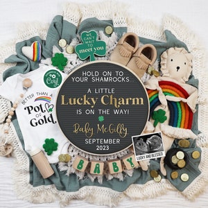 Puede incluir: Un tablero de letras blanco y negro con el texto "Hold on to your shamrocks... A little Lucky Charm is on the way! Baby Mc Gilly September 2023". El tablero de letras está rodeado de una manta verde, un arcoíris, un body de bebé y monedas de oro.