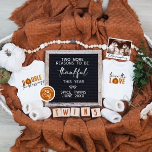 May include: A fall-themed baby announcement featuring two white babygrows, one with the text "Double the Blessings" and the other with the text "Twice the Love". A black letter board with the text "Two more reasons to be thankful this year. Spice Twins June 20XX" is in the centre of the image. The babygrows and letter board are in a wicker basket with a brown blanket, white beads, and a small green plant.