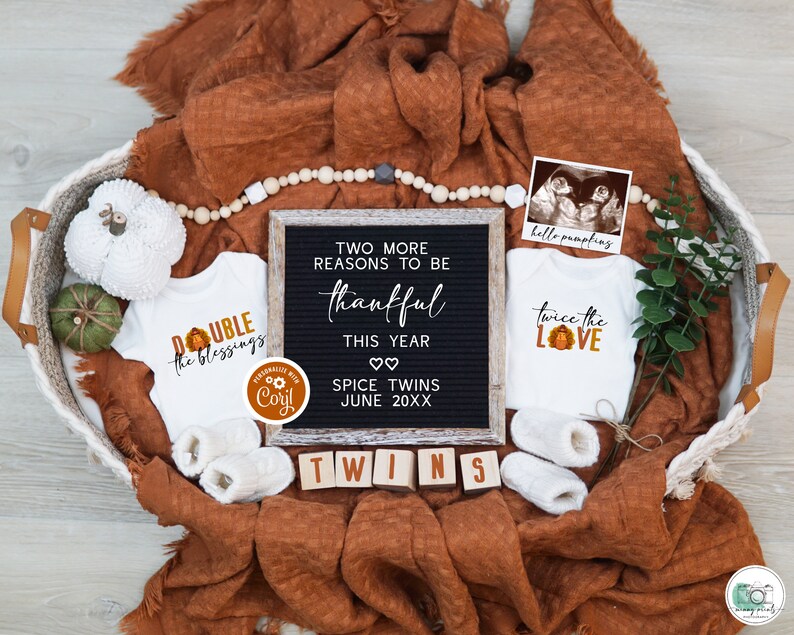 May include: A fall-themed baby announcement featuring two white babygrows, one with the text "Double the Blessings" and the other with the text "Twice the Love". A black letter board with the text "Two more reasons to be thankful this year. Spice Twins June 20XX" is in the centre of the image. The babygrows and letter board are in a wicker basket with a brown blanket, white beads, and a small green plant.