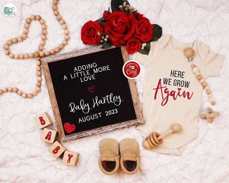 K&ouml;nnte beinhalten: Ein schwarzes Buchstabenbrett mit dem Text "Adding a little more love" und "Baby Hartley August 2023". Ein rotes Herz befindet sich neben dem Text. Ein wei&szlig;er Strampler mit dem Text "Here we grow again" in Rot. Eine Holzrassel und ein Paar braune Babyschuhe sind ebenfalls im Bild.