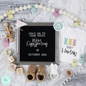 Peut inclure: Un panneau d'annonce en ardoise avec le texte "Hold on to your peeps We're Eggspecting October 2022" et un body blanc avec trois poussins jaunes pastel et le texte "Baby Harlow".