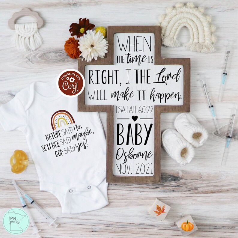 May include: A wooden cross with the text "WHEN THE TIME IS RIGHT, I THE LORD WILL MAKE IT HAPPEN. ISAIAH 60:22" and "BABY Osborne NOV. 2021". A white onesie with the text "NATURE SAID NO. SCIENCE SAID MAYBE. GOD SAID YES!" and a rainbow graphic.
