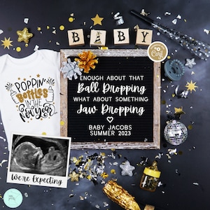 May include: A black and white ultrasound image of a baby in a white frame with the text "We're Expecting". A white onesie with gold lettering that says "Poppin' Bottles in the New Year". A black letter board with the text "Enough about that Ball Dropping. What about something Jaw Dropping. Baby Jacobs Summer 2023".