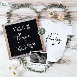 May include: A black letter board with the text "Soon to be a family of three" and "Due to arrive August 202X". A white onesie with the text "Baby Hurley" and a black heart. A white ultrasound image with the text "Coming Soon".