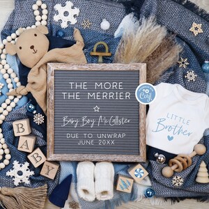 May include: A blue and white blanket with a letter board that reads "The More The Merrier Baby Boy McCallster Due To Unwrap June 20XX". There is a white onesie with the text "Little Brother" and a brown teddy bear with a blue and white blanket.