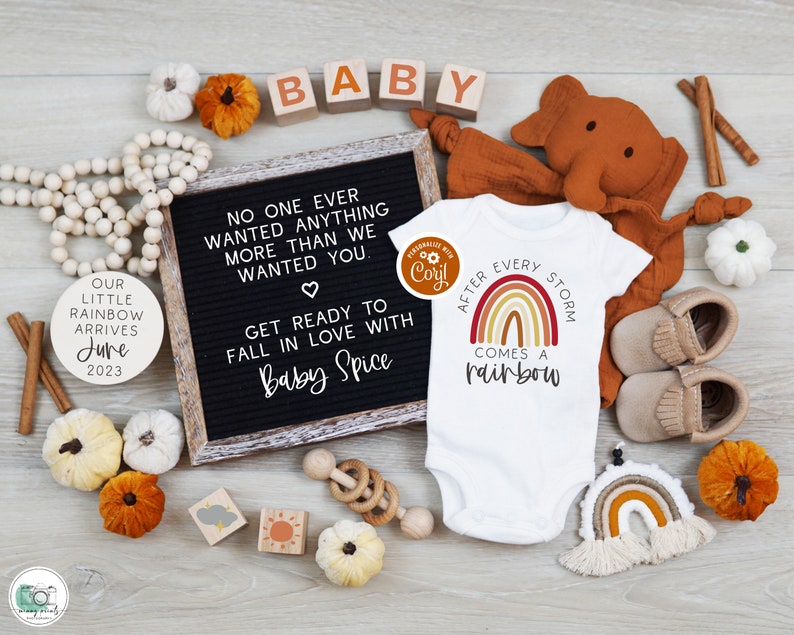 May include: A baby announcement with a letter board that reads "No one ever wanted anything more than we wanted you."  The board is surrounded by fall-themed decorations, including pumpkins, cinnamon sticks, and a wooden elephant. The announcement also includes a white onesie with the text "After every storm comes a rainbow" and a rainbow graphic.