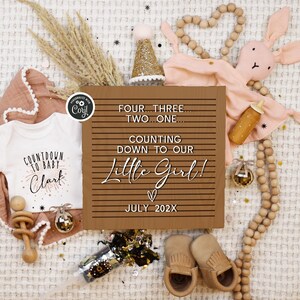 May include: A brown wooden sign with white text that reads "Four...Three...Two...One...Counting down to our Little Girl!  ♡ July 202X".  The sign is surrounded by baby items, including a white onesie with the text "Countdown to Baby Clark", a pink bunny rattle, a wooden rattle, and a gold party hat.