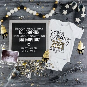 May include: A black and white ultrasound image with the text "Our Little Big News" below it. A framed chalkboard with the text "Enough about that ball dropping, how about something jaw dropping? Baby Allen July 202X". A white onesie with the text "We're expecting 202X to be great!!" in gold glitter. A gold bottle with a black bow and a gold bottle with a black bow. A black and white garland with white pom poms. Gold and silver confetti.