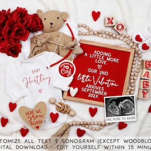 Könnte beinhalten: Ein rot-weißes Baby-Bodysuit mit dem Text "Baby Hartley" und einem roten Herz. Eine rote Buchstaben-Tafel mit dem Text "Adding a little more love. Our 2nd little Valentine arrives September 202X". Ein Teddybär, der einen Bogen und Pfeil hält. Rote Filzherzen, Holzblöcke, die "BABY" buchstabieren, und eine Holzperlenkette.