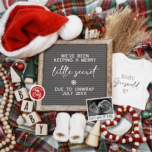 Op de afbeelding: Een zwangerschapsaankondiging met kerstthema met een letterbord waarop staat "We've been keeping a merry little secret due to unwrap July 20XX". Naast het letterbord ligt een wit rompertje met de tekst "Baby Griswold". Een kerstmanmuts, houten blokken die "BABY" spellen, een baby-echobeeld en andere kerstversiering zijn verspreid rond het letterbord en het rompertje.