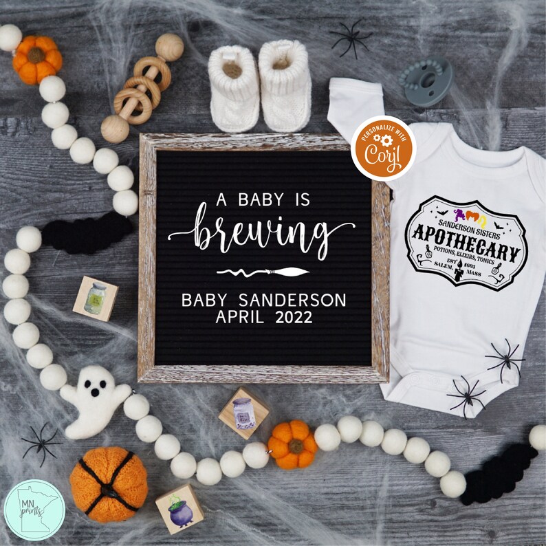 May include: A black letter board with the text "A baby is brewing, Baby Sanderson, April 2022". A white onesie with the text "Sanderson Sisters Apothecary, Potions, Elixirs, Tonics, Est. 1693, Salem, Mass."  A white ghost, a pumpkin, and a cauldron are on a gray surface with white spider webs.