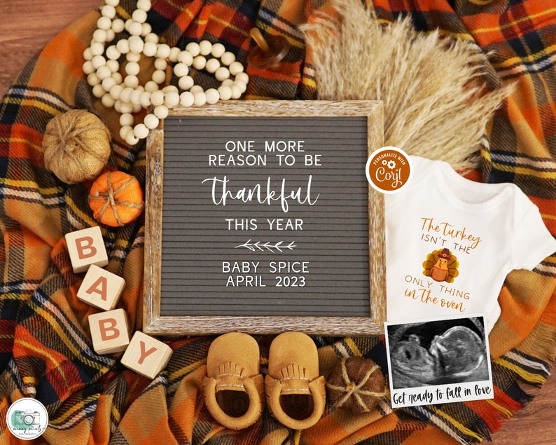 K&ouml;nnte beinhalten: Eine Baby-Ank&uuml;ndigung im Herbst-Stil mit einer Buchstaben-Tafel, auf der steht "One more reason to be thankful this year Baby Spice April 2023". Es gibt Holzbl&ouml;cke, die "BABY" buchstabieren, ein Paar braune Baby-Mokassins, einen kleinen wei&szlig;en Strampler mit einem Truthahn-Motiv und dem Text "The Turkey isn't the only thing in the oven" und ein gerahmtes Ultraschallbild.