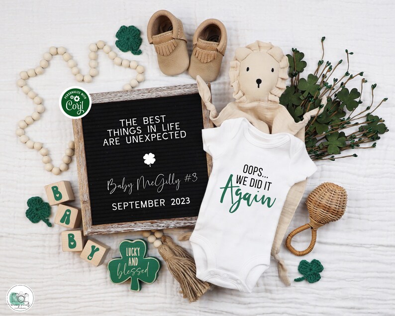 May include: A white onesie with green text that reads "Oops... We Did It Again". The onesie is surrounded by a variety of green shamrocks, a wooden rattle, a stuffed lion, and a letter block spelling "Baby". A black letter board with white text reads "The Best Things In Life Are Unexpected Baby McGilly #3 September 2023".