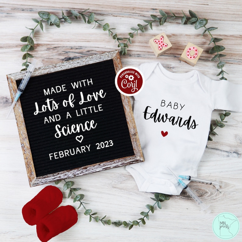 May include: A black letter board with the text "MADE WITH Lots of Love AND A LITTLE Science FEBRUARY 2023". A white onesie with the text "BABY Edwards" and a red heart. Two red booties and two wooden blocks with the letters "X" and "O" are also in the image.