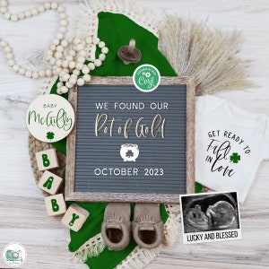 Może przedstawiać: Szara tablica z literami z tekstem "WE FOUND OUR Pot of Gold OCTOBER 2023".  Okrągły drewniany znak z tekstem "BABY Mabely" i koniczyną.  Biały śliniaczek z tekstem "GET READY TO Fall in Love" i koniczyną.  Czarno-białe zdjęcie USG z tekstem "LUCKY AND BLESSED".  Para brązowych mokasynów dla niemowląt.  Zielona tkanina z białą koronką.  Drewniane klocki układające się w słowo "BABY".