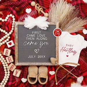 K&ouml;nnte beinhalten: Eine rot-wei&szlig; karierte Decke mit einem wei&szlig;en Strampler, auf dem "BABY Hartley" in roter Schrift steht. Es gibt eine Buchstabentafel, auf der "FIRST CAME LOVE, THEN ALONG CAME YOU" mit einem Herz und "JULY 20XX" steht. Es gibt Holzbl&ouml;cke, die "BABY" buchstabieren, und eine Holzrassel.