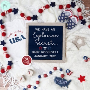 May include: A patriotic baby announcement with a white onesie that says "made in the USA." A letter board reveals "We Have an Explosive Secret... BABY ROOSEVELT JANUARY 2022." Red, white, and blue decorations include star-shaped booties and a garland.
