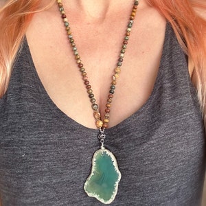 May include: A long necklace with a green agate pendant. The necklace is made of small, multi-colored beads.