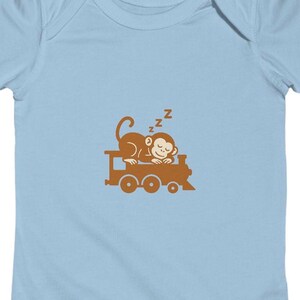 May include: Light blue baby onesie featuring a brown cartoon monkey sleeping on a brown train. The monkey has the letter "Z" above its head, indicating sleep. The onesie is made of soft material.