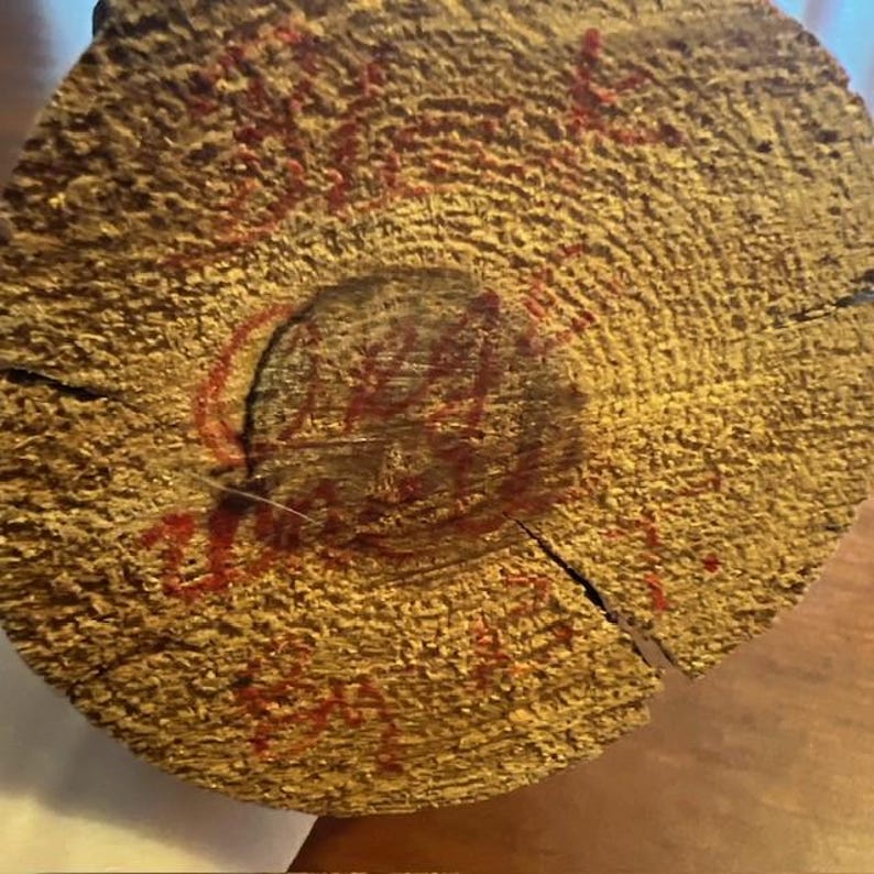 May include: Close-up of a cross-section of a tree trunk, showcasing the wood's texture and growth rings. Red markings are visible on the surface, possibly handwritten text or a stamp. The wood has a light brown color.
