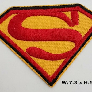 Könnte beinhalten: Gestickter Superman-Logo-Patch in Rot und Gelb mit schwarzem Umrandung. Der Patch ist 7,3 cm breit und 5 cm hoch.