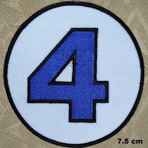 Può includere: Un cerotto circolare bianco con un contorno nero, su cui è ricamato un numero "4" blu. Il cerotto ha un diametro di 7,5 cm.