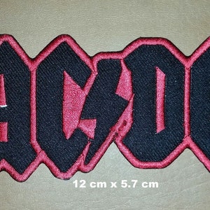 May include: Black and red embroidered iron-on patch with the word "AC/DC" in a stylized font. The patch is 12 cm x 5.7 cm.