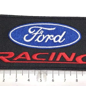 Könnte beinhalten: Schwarzer gestickter Aufnäher mit einem blauen Oval, das das Wort "Ford" in weißen Buchstaben und das Wort "RACING" in roten Buchstaben darunter enthält.