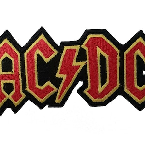 May include: A black and red embroidered patch with the word "AC/DC" in a bold, stylised font. The letters are outlined in gold.