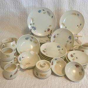 May include: A set of vintage ceramic dinnerware with a leaf and flower pattern in shades of brown, blue, and green. The set includes plates, bowls, and cups.