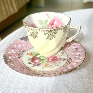May include: A delicate teacup and saucer set with a floral design. The teacup is white with gold trim and features a pink rose. The saucer is pink with a lace-like edge and a floral pattern.