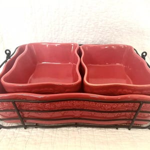 May include: A red ceramic baking dish set with a black metal rack. The dish is divided into two sections and has a scalloped edge.