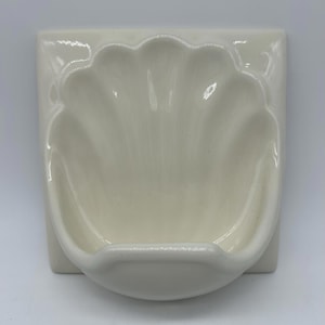 Peut inclure: Porte-savon en céramique blanc cassé en forme de coquillage. Le porte-savon est monté sur un carreau carré, avec un motif festonné formant la coquille. Le porte-savon a une finition lisse et brillante.