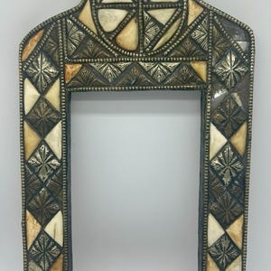 May include: A rectangular picture frame with a pointed arch top, featuring an alternating pattern of cream-coloured bone inlays and dark, etched metal diamond-shaped tiles. The frame is bordered by a thin, beaded metal trim along the edges.