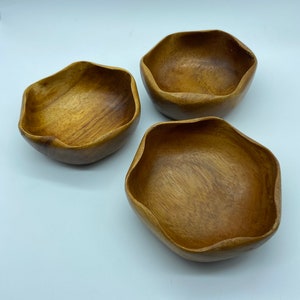 May include: Three wooden bowls with a natural wood finish. The bowls are all the same size and shape, and they have a slightly irregular, wavy edge.