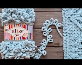 May include: A skein of light blue Alize Puffy Fine yarn with a label that reads "Soft & Quick Alize Puffy Fine Patent". The yarn is shown next to a crocheted blanket and a crocheted chain.