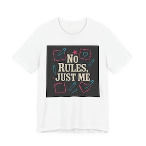 Puede incluir: Camiseta blanca con un diseño gráfico que presenta el texto "NO RULES, JUST ME". El diseño incluye formas rosas y azules, imperdibles y una estrella. La camiseta es una prenda informal para el día a día.