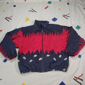 May include: A blue and red windbreaker jacket with a zipper closure and a white pattern. The jacket has a drawstring at the bottom.