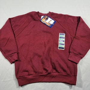 May include: A maroon sweatshirt with a crew neck and long sleeves. The sweatshirt has a tag attached with the word "Medium" printed on it.